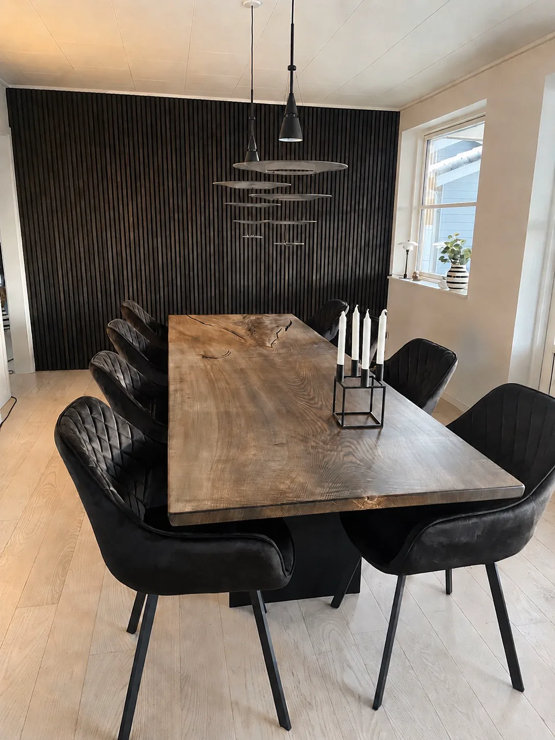 Karakterfuldt plankebord med sorte stole foran en mørk trævæg